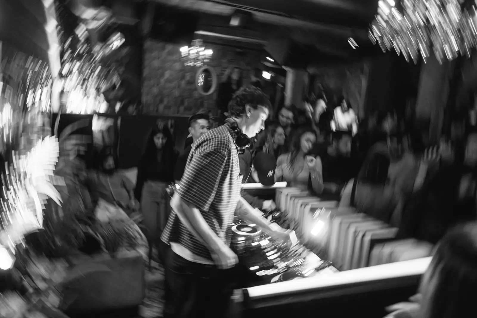 A DJ at the decks in a busy room, in black and white